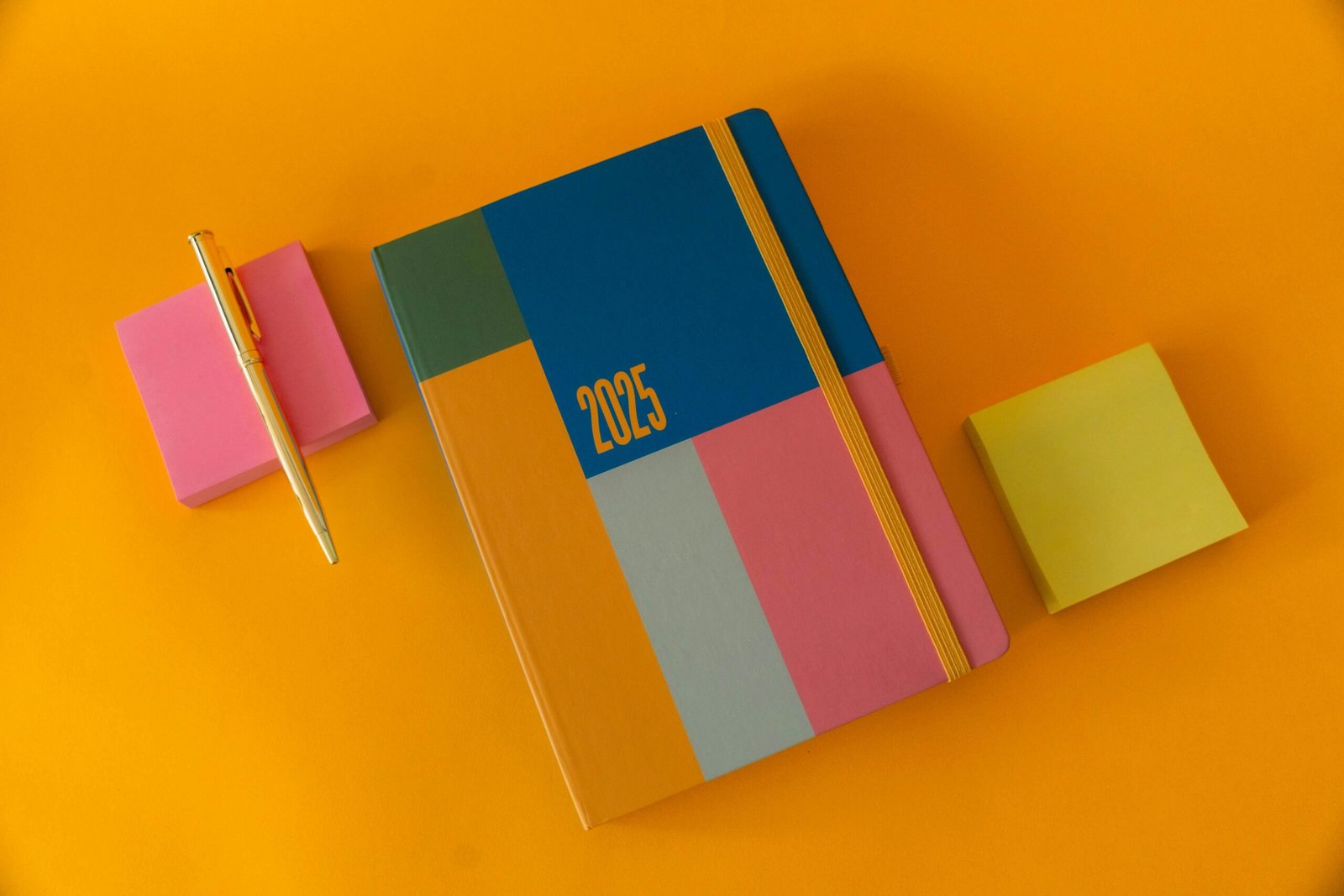 Vibrant flat lay of a 2025 planner with sticky notes and a pen on an orange background.
